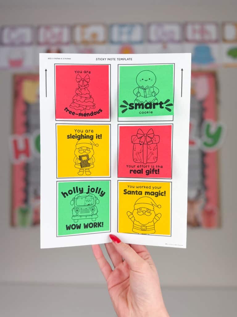 A hand holds a printed sheet of Christmas classroom decor sticky note templates featuring colorful 3x3 positive notes with festive designs, including Santa, gingerbread, gifts, and trees, and cheerful messages like “You are tree-mendous,” “Smart cookie,” “You are sleighing it,” and You worked your Santa magic!” The background shows a blurred holiday bulletin board.